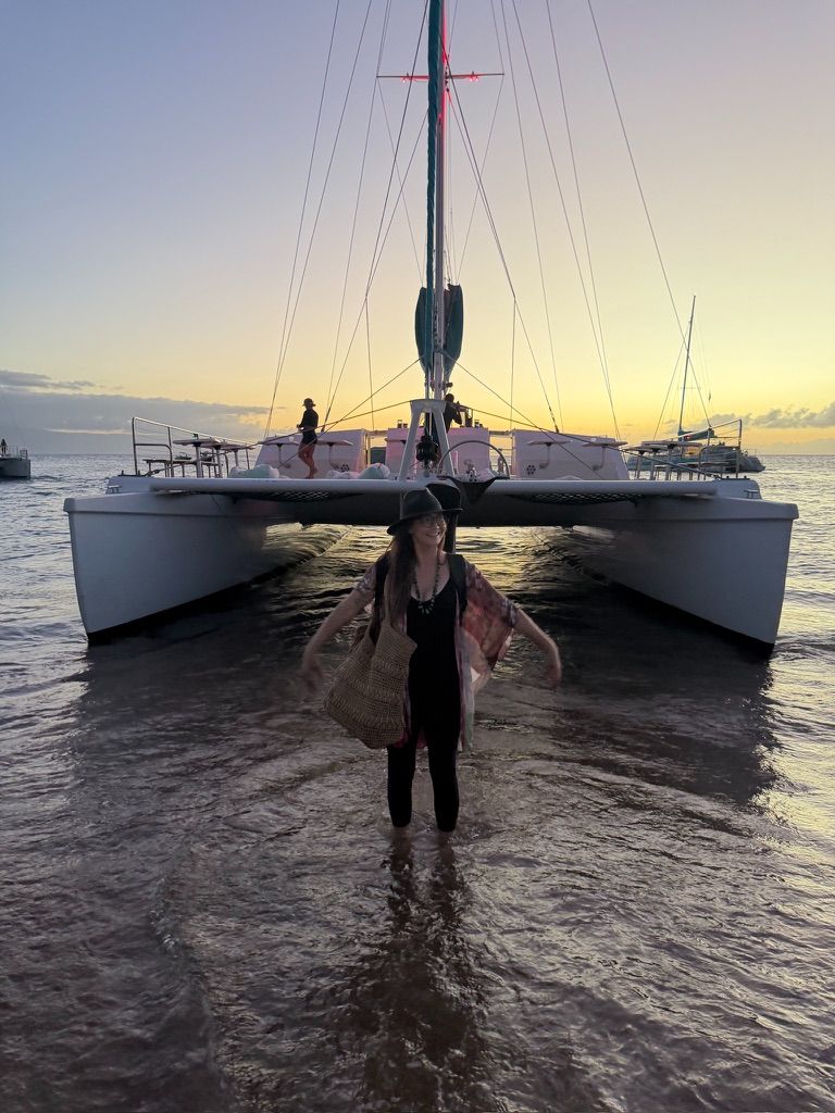 Kris Bradley standing in the water in front of a catamaran at sunset on Maui.
