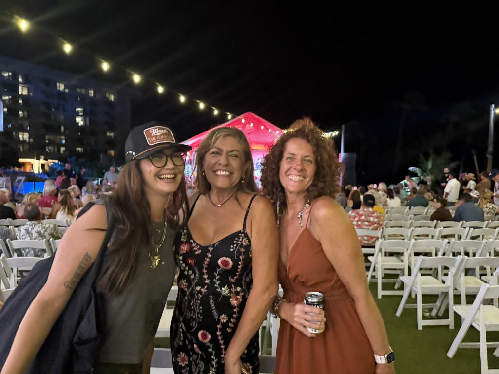 Kris Bradley smiling with friends at an outdoor evening event on Maui, string lights overhead.