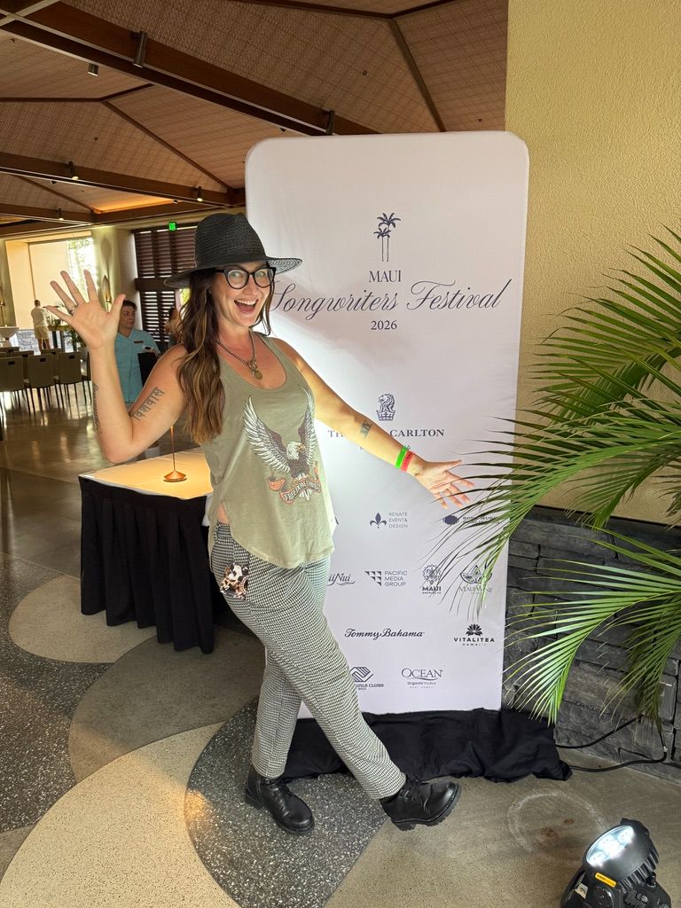 Kris Bradley posing in front of the Maui Songwriters Festival sign.
